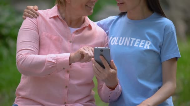 Mujer anciana feliz mostrando fotos de teléfonos inteligentes a voluntarios jóvenes, comunicación — Vídeo de stock