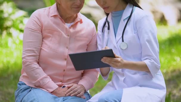 Genç doktor, yaşlı kadın hastanın teşhisini tartışan tablette görüntüleri gösteriyor — Stok video
