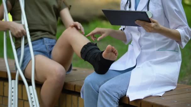 Médica do sexo feminino aconselhando paciente perna quebrada na cinta do tornozelo sufocando raio-X em comprimido — Vídeo de Stock