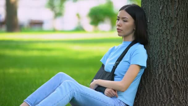 Giovane signora con braccio ferito in supporto fionda seduta albero nel parco, medicina — Video Stock