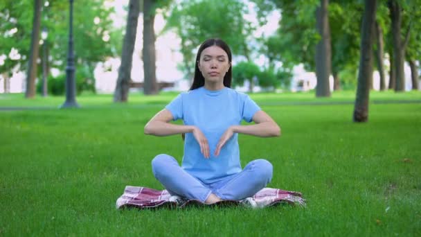 Atractiva joven dama meditando en el parque sentado pose de loto, relajante al aire libre — Vídeo de stock