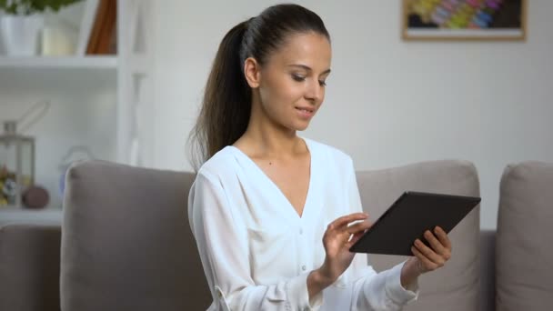 Young woman using tablet PC at home, looking at camera, social network, online — Stock Video