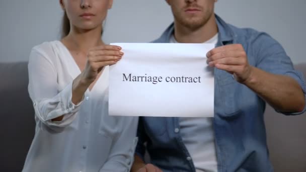 Serious couple tearing into pieces marriage contract phrase on cardboard — Stock Video