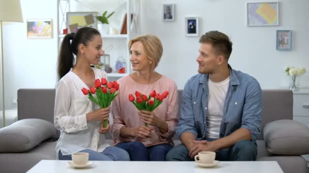 Hombre abrazando madre y esposa sosteniendo tulipanes, sonriendo a la cámara, regalo de vacaciones — Vídeo de stock