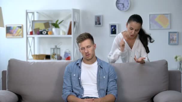 Нервная женщина критикует ленивого мужа, сидящего на диване, семейный конфликт, проблему — стоковое видео