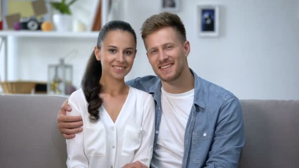 Couple joyeux assis sur le canapé, montrant les mains avec des bagues de fiançailles, amour — Video