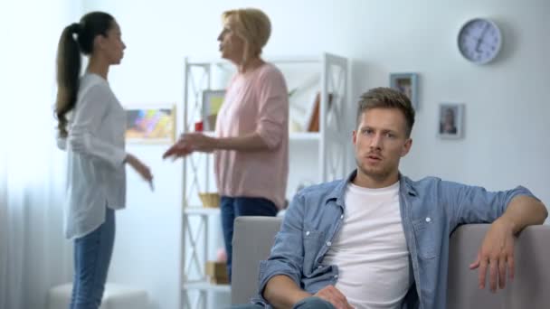 Несчастный мужчина сидит дома на диване и слушает, как жена ссорится с матерью. — стоковое видео