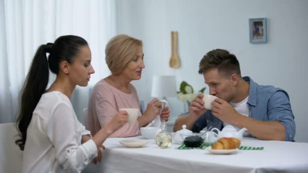 Shocked wife looking at mother-in-law putting napkin on husbands neck, tea party — Stock Video
