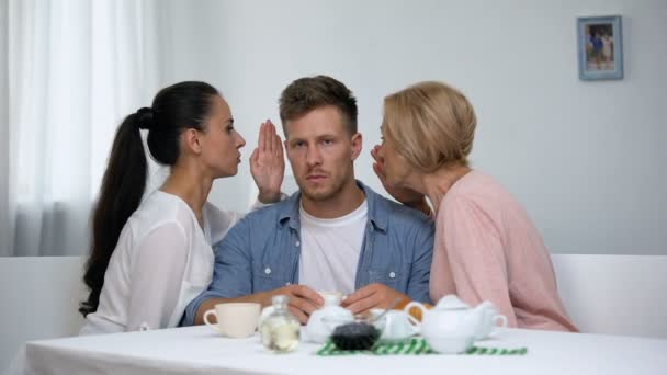 Запутавшийся мужчина слушает жену и мать шепчет советы на ухо, отношения — стоковое видео