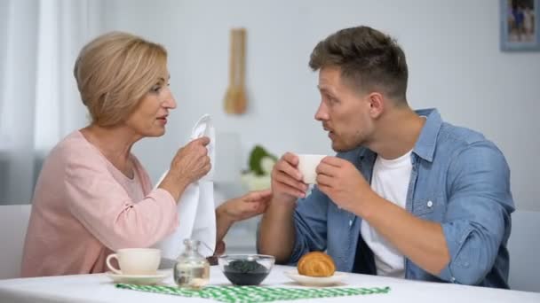 お茶を飲みながら息子の首にナプキンを置く注意深い母親、過剰保護 — ストック動画