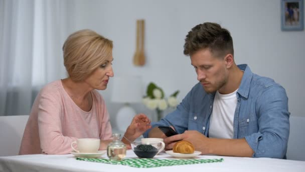 Worried mother talking to infantile adult son playing video games on smartphone — Stock Video