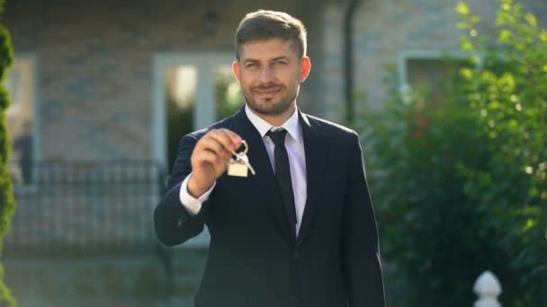 Sonriente agente de bienes raíces sosteniendo en la mano la llave de la casa, esperando a los clientes — Vídeo de stock