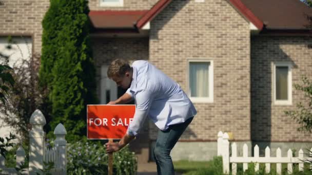 Glücklicher Hausbesitzer, der vor dem Gebäude ein Schild zum Verkauf anbringt, zieht um — Stockvideo