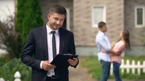 Smiling broker standing with documents, happy family hugging near their new home — Stock Video