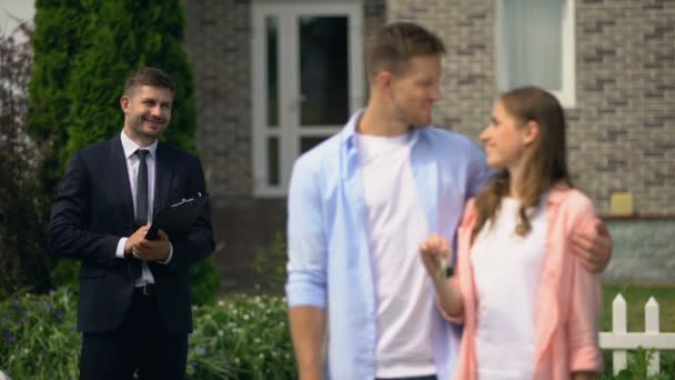 Agente inmobiliario viendo feliz pareja disfrutando de la nueva casa mostrando las llaves de la cámara — Vídeos de Stock