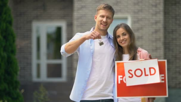 Happy family couple smiling, holding house keys standing near sold signboard — Stock Video