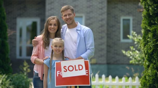 Glückliche Familie hält Schild verkauft, steht gegen neu gekauftes Haus, Daumen hoch — Stockvideo