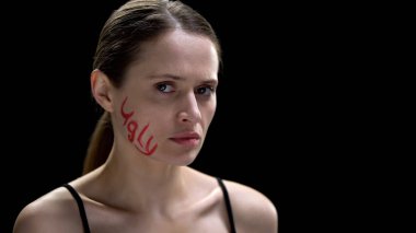 Kameraya bakarak yanak üzerine yazılmış çirkin kelime ile Üzgün kadın, düşük benlik saygısı