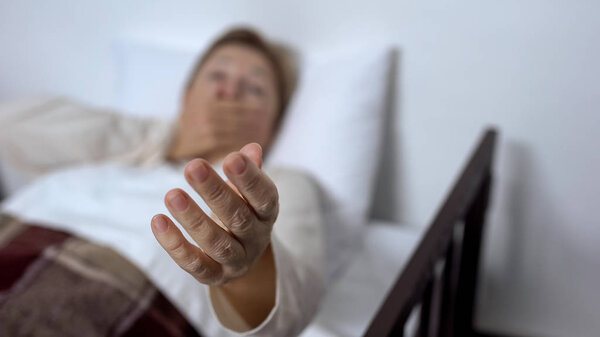 Ill senior female patient lying in sickbed, hardly breathing and asking for help