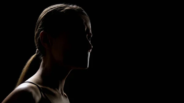 Young woman with taped mouth against black background, slavery and humiliation