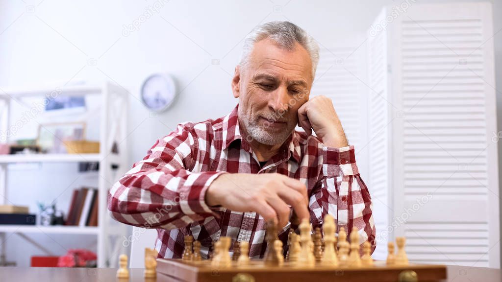 Happy senior man playing chess alone, training for chess competition, checkmate