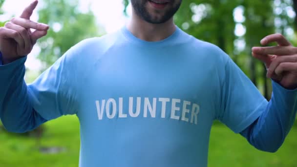 Hombre sonriente señalando palabra voluntaria en camiseta, preservación de la vida silvestre, tierra — Vídeo de stock