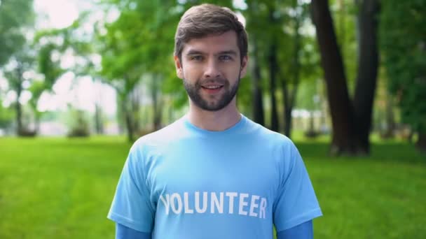 Счастливый мужчина-активист, указывающий на добровольное слово на голубой футболке, эко-проект — стоковое видео