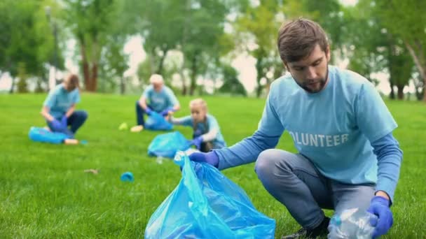 Щасливий чоловік-доброволець кладе сміття в мішок для сміття і посміхається, відповідальний — стокове відео