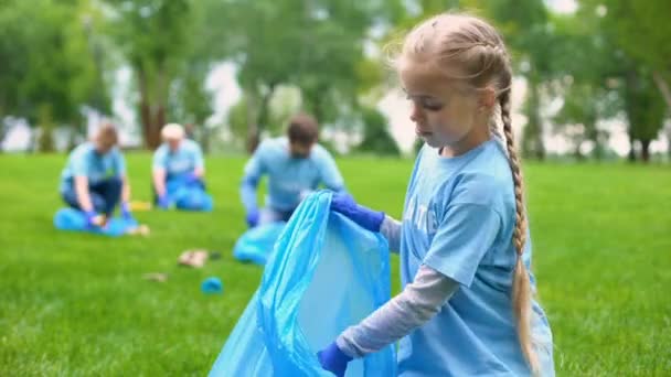 Ответственный ребенок-волонтер собирает мусор в мешок для мусора, улыбаясь на камеру — стоковое видео