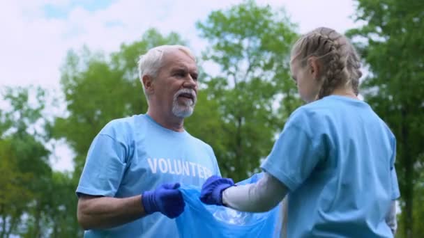 Souriant volontaire âgé avec petite-fille collecte des ordures donnant haute cinq — Video