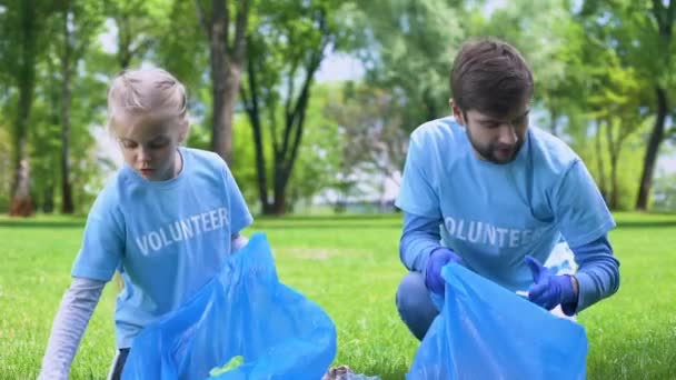 Μαθήτρια μαζί με τον πατέρα μαζεύοντας απόβλητα πάρκο σε σακούλες χαμογελώντας ο ένας τον άλλο — Αρχείο Βίντεο