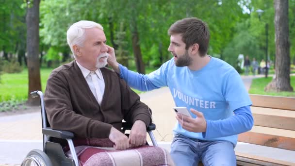 Positiver männlicher Ehrenamtlicher unterhält behinderten Patienten, hört gemeinsam Musik — Stockvideo