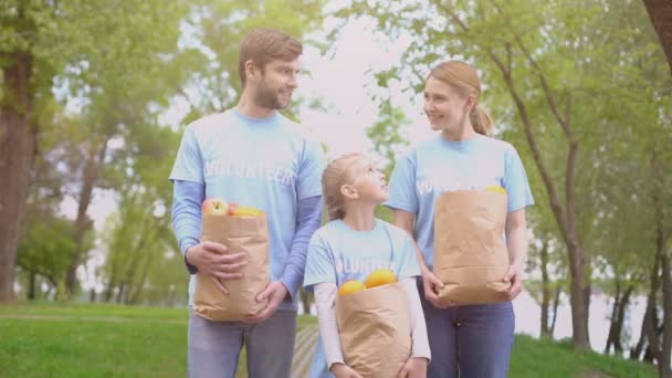 Manliga kvinnor och barn volontärer innehar papperspåsar med frukt, leende kamera — Stockvideo