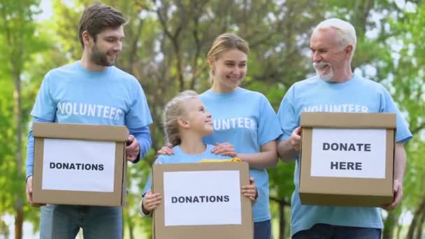 Усміхнені добровольці, які тримають пожертвування, дивляться камери, благодійний проект, допомагають — стокове відео