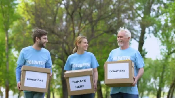 Des activistes heureux avec des boîtes de dons marchant dans le parc, fondation caritative, aide — Video