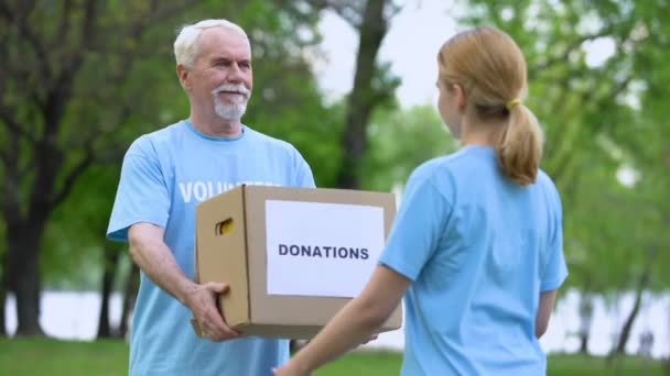 幸せな高齢ボランティアが寄付箱を寄付する若い女性、人道支援、慈善団体 — ストック動画