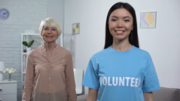 Activista social femenina mostrando pulgares hacia arriba con la señora mayor alegre en el fondo — Vídeos de Stock