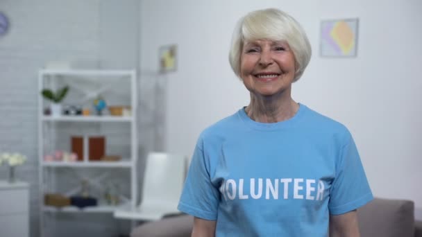 Χαμογελαστή ηλικιωμένη κυρία στο μπλουζάκι εθελοντών με κάμερα, φιλανθρωπικός οργανισμός — Αρχείο Βίντεο