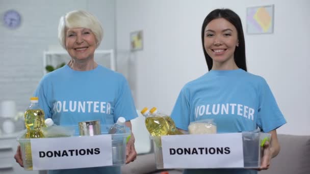 Sonriendo voluntarios mayores y jóvenes sosteniendo cajas de donación de alimentos mirando la cámara — Vídeo de stock