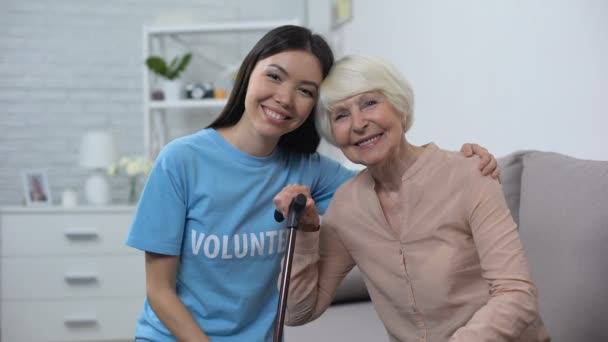 Młody żeński ochotnik przytulanie dojrzały emeryci chodzenie trzymać uśmiechnięty aparat fotograficzny — Wideo stockowe