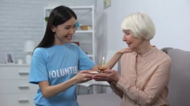 Huzurevinde ki kıdemli emekliye doğum günü pastası sunan gülümseyen gönüllü