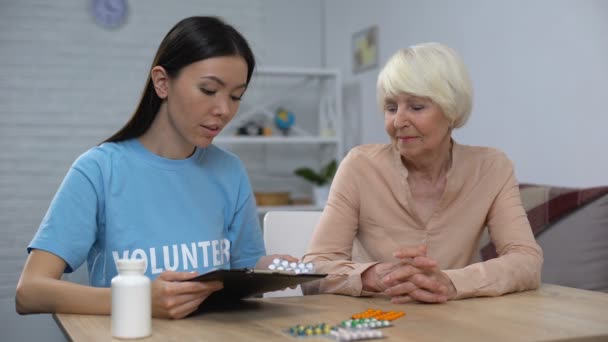 Giovane volontaria lettura prescrizione e dando pillole alla signora anziana, aiuto — Video Stock
