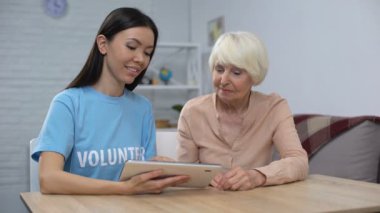 Yaşlı emekliyi gösteren kadın gönüllü tablet uygulamasını kullanmak için gülümseyen kamera