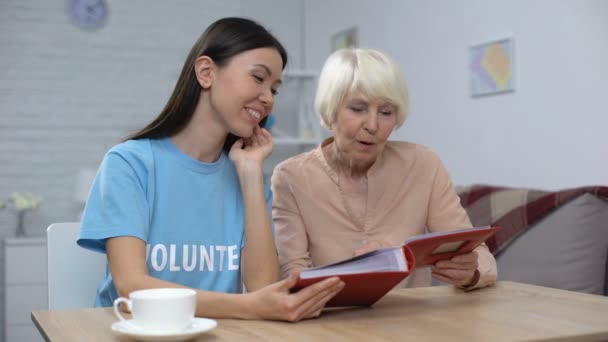 Érett nő mutatja női önkéntes fotóalbumot, idősek otthonában szabadidő, gondozás — Stock videók