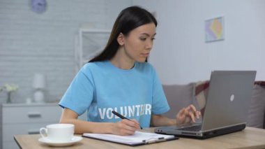 Kadın gönüllü çalışma dizüstü bilgisayar ve yazma notları oturma masası, hayır projesi