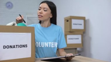 Genç gönüllü kıyafet bağış kutusunu kontrol ediyor ve not alıyor, insani yardım