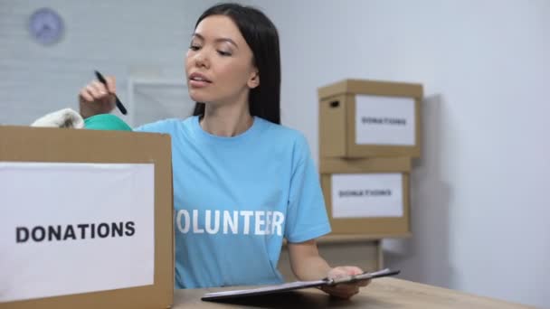 Jovem voluntária checando caixa de doação de roupas e fazendo anotações, ajuda humanitária — Vídeo de Stock