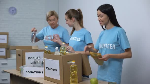 Glada kvinnor i volontär t-shirts sätta konserverad matlådor, tillhandahållande donation — Stockvideo