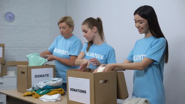 Activista social femenina preparando cajas de donaciones con ropa y cámara sonriente — Vídeo de stock