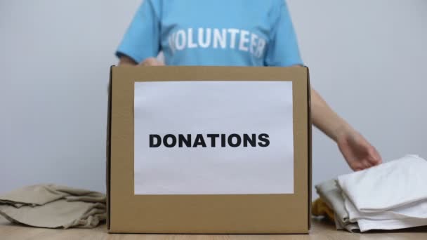 Tipo ativista do sexo feminino colocando roupas em caixa de doação na mesa, cuidado orfanato — Vídeo de Stock